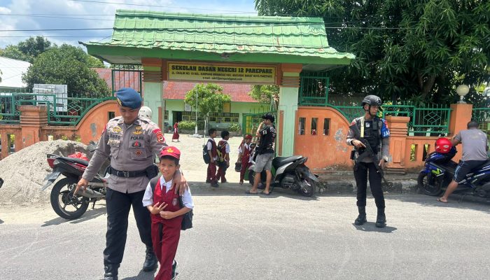 Personel Brimob Batalyon B Pelopor Satuan Brimob Polda Sulsel Bantu Anak Sekolah Menyebrangi Jalan Padat Kendaraan